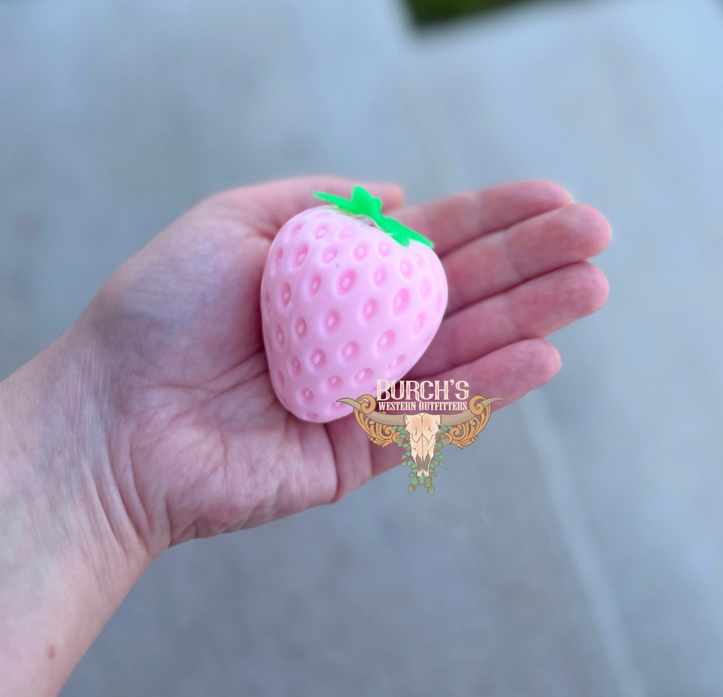 Pink strawberry-shaped object held in a hand with a blurred background