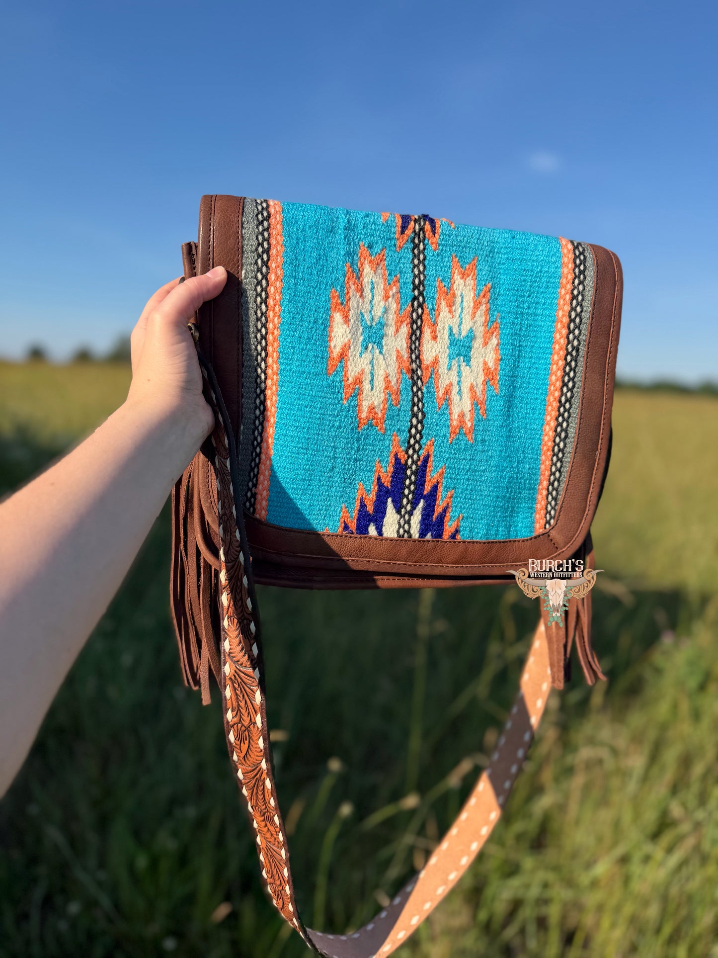 Handbag with a colorful pattern held in front of a grassy field