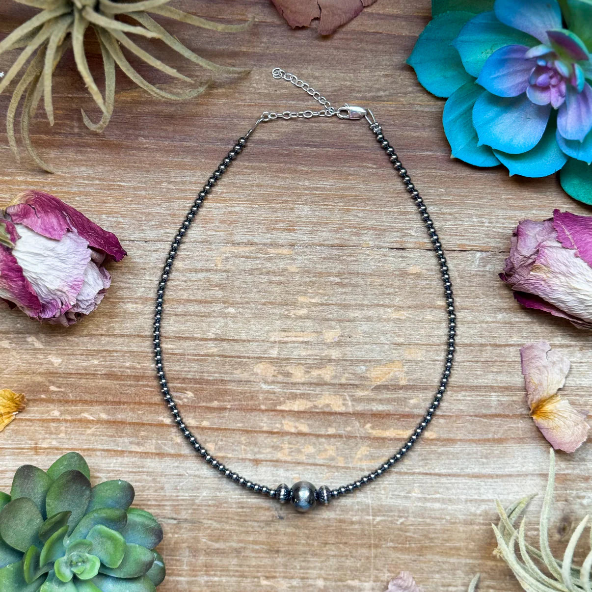 Necklace on a wooden surface with flowers and plants