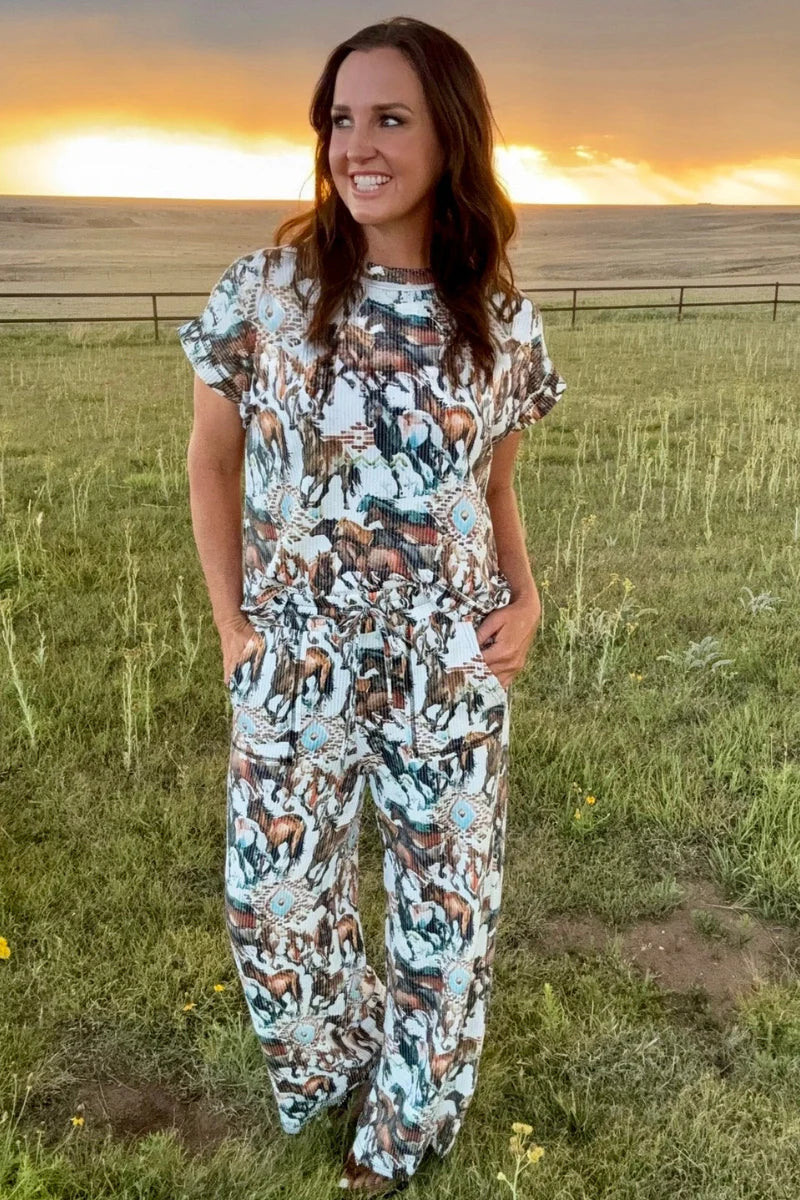 Woman in a patterned outfit standing in a field with a sunset in the background
