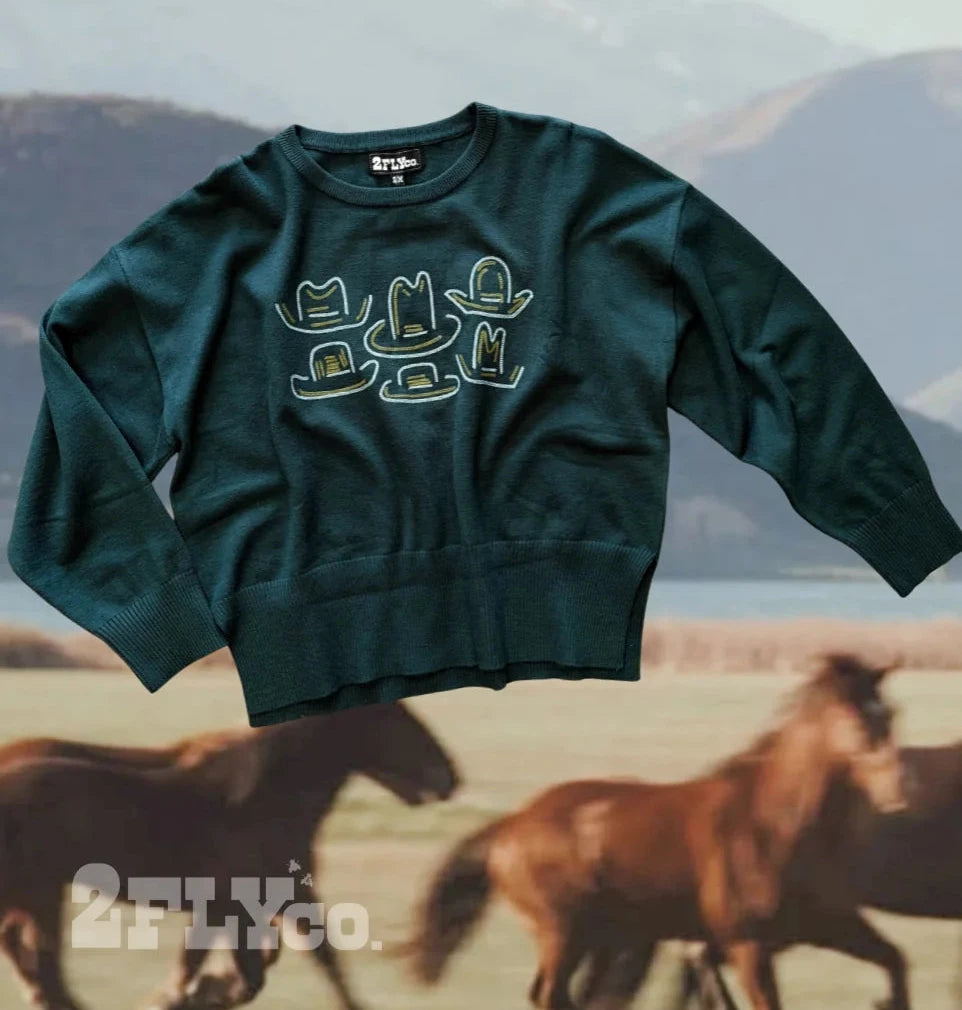 Dark green western sweater featuring embroidered cowboy hat designs in cream and gold on the front, styled against a scenic background with running horses.