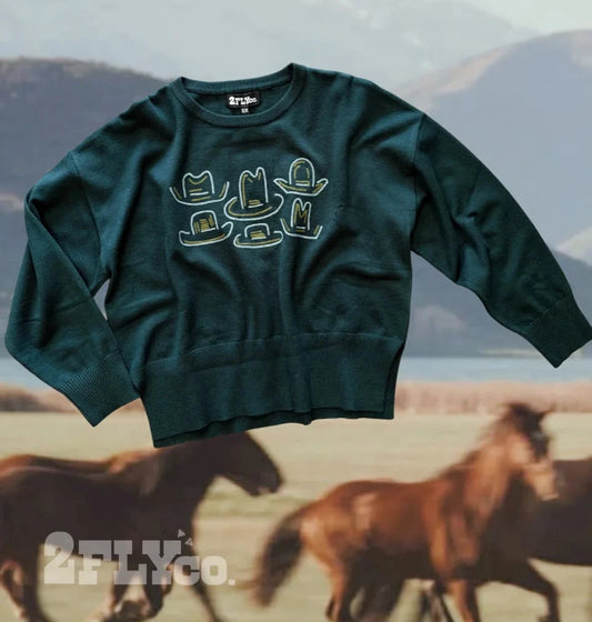 Dark green western sweater featuring embroidered cowboy hat designs in cream and gold on the front, styled against a scenic background with running horses.