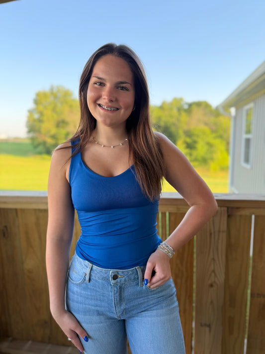Woman in a blue tank top and jeans standing on a deck with a scenic background