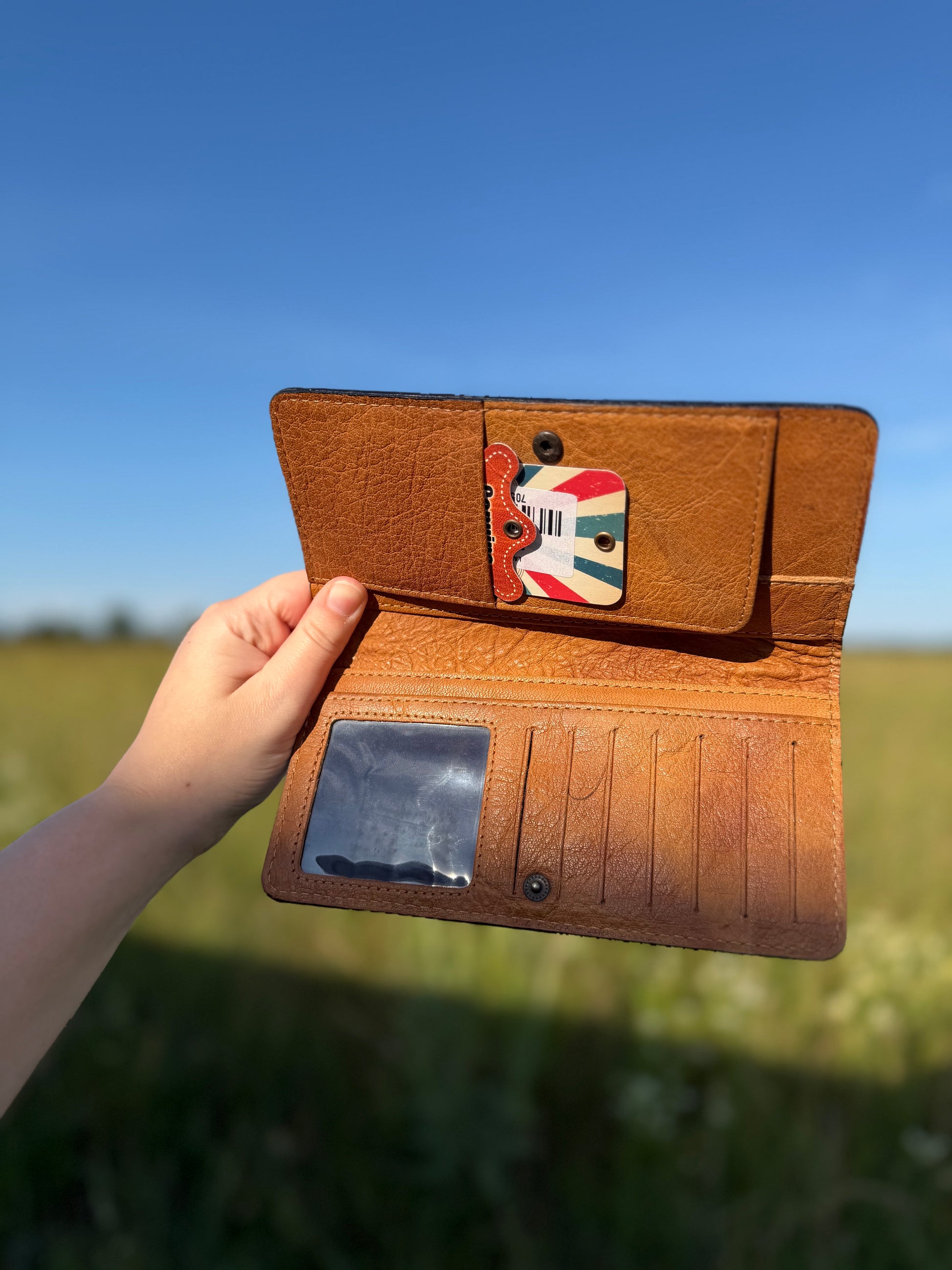 Brown leather wallet held open with a field and blue sky in the background