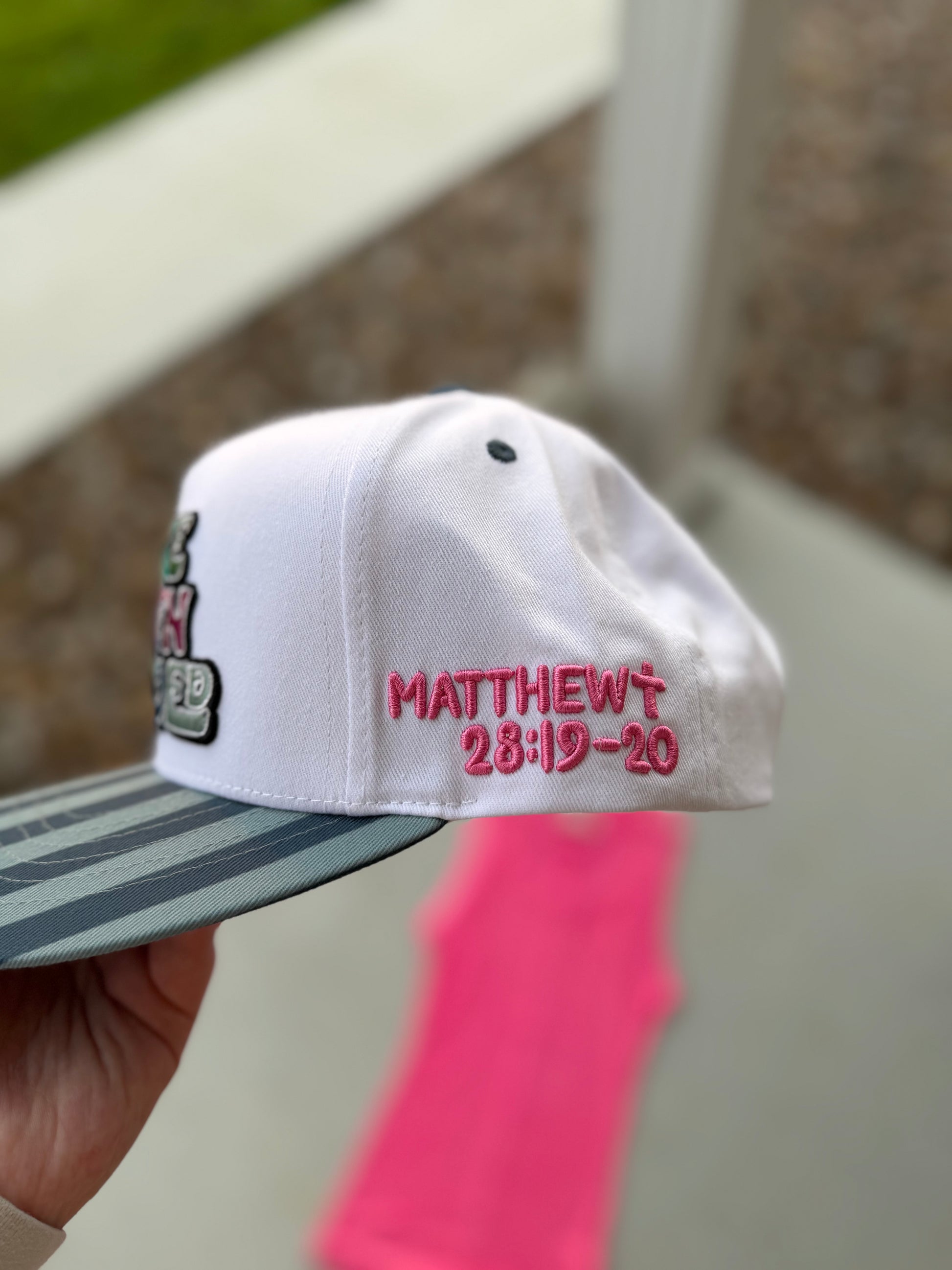 White cap with embroidered text held by a hand against a blurred background