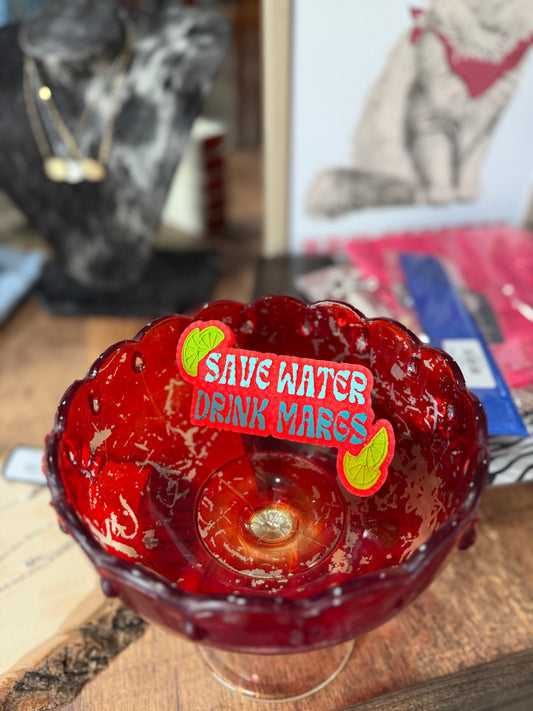 Red glass bowl with a 'Save Water Drink Mars' freshie on a wooden surface