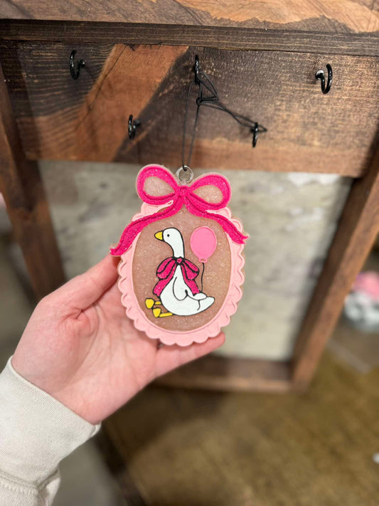 Decorative Freshie with a pink duck design held by a hand against a wooden background