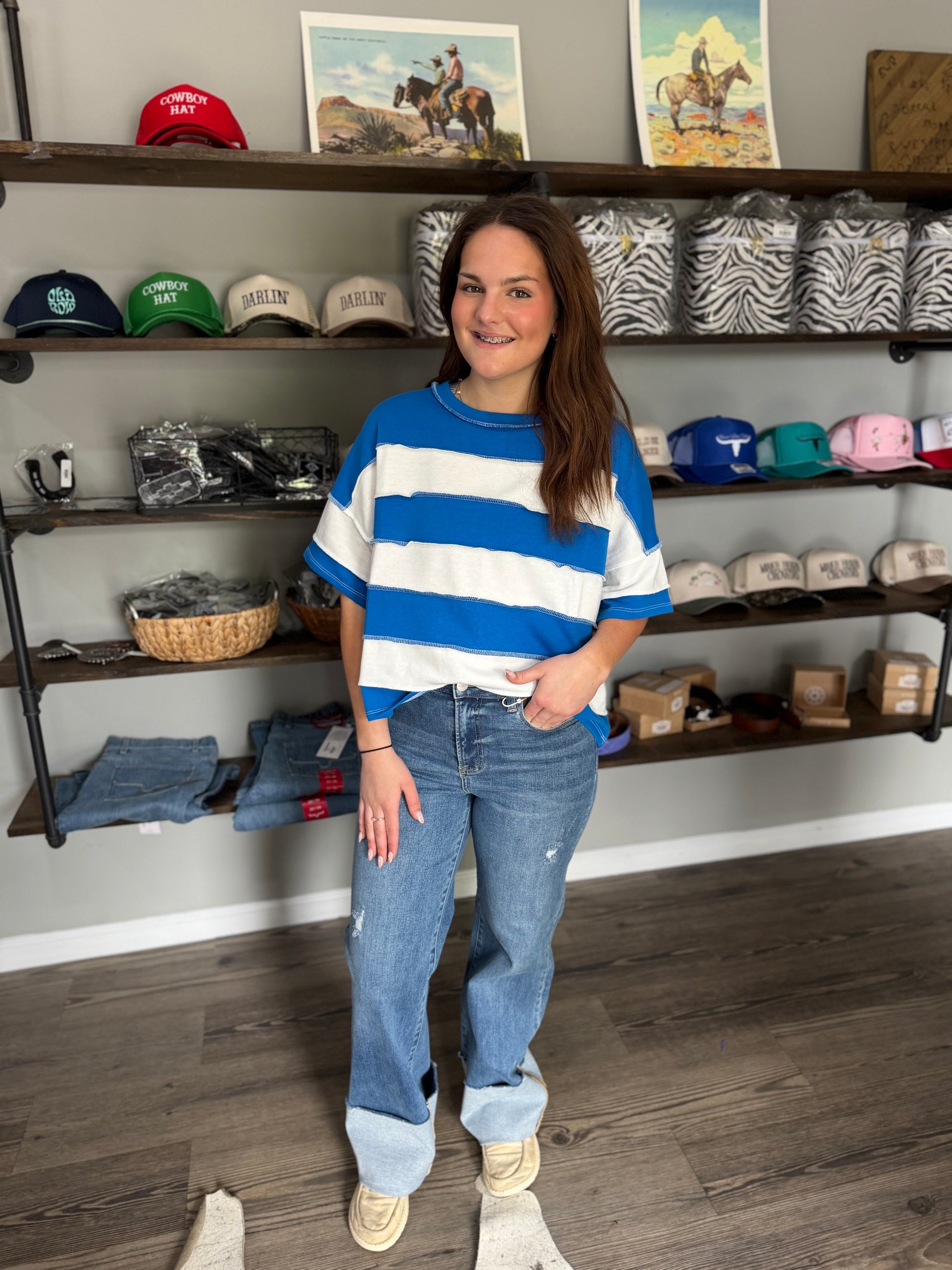 Woman in a striped sweater and jeans standing in a store with shelves of merchandise.