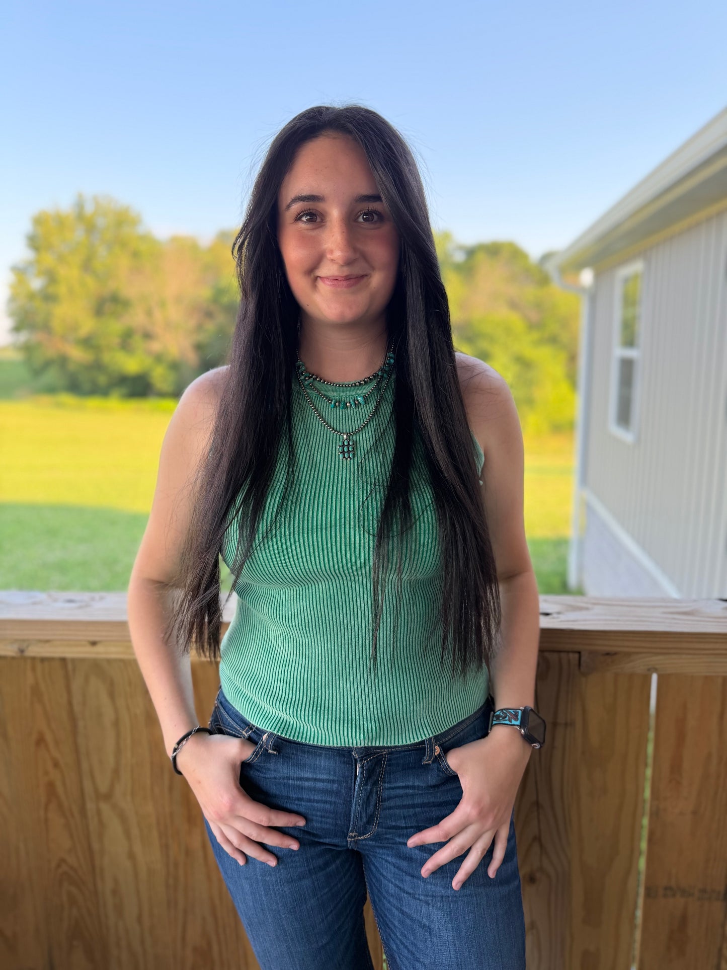 Woman standing on a deck with a scenic background of trees and open field.