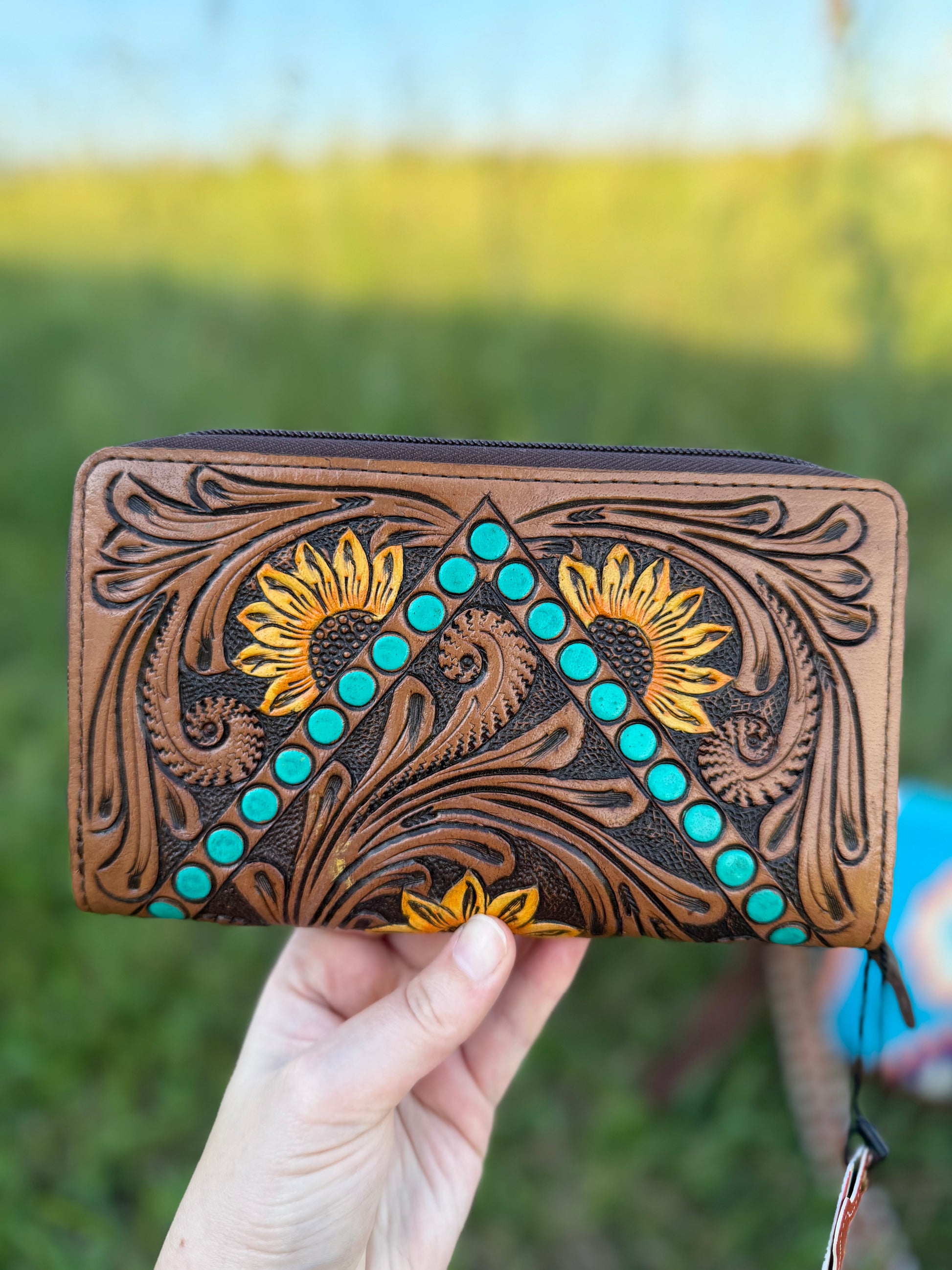 Handmade leather wallet with floral patterns and turquoise stones held against a blurred natural background
