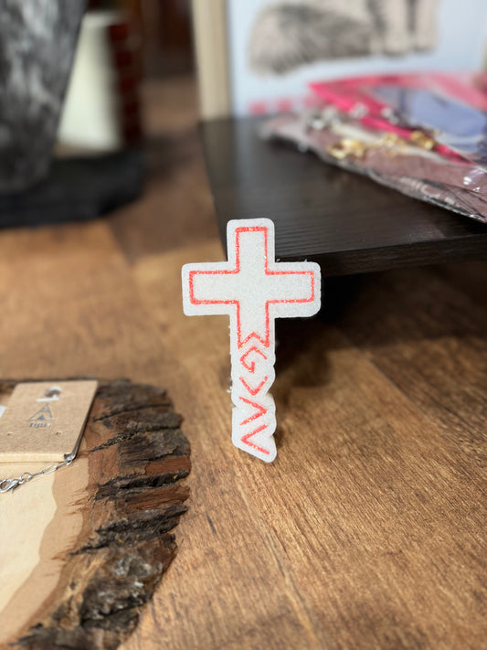 Cross-shaped freshie with red accents on a wooden surface