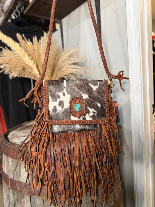 Fringe handbag with cowhide pattern and turquoise stone on a wooden barrel