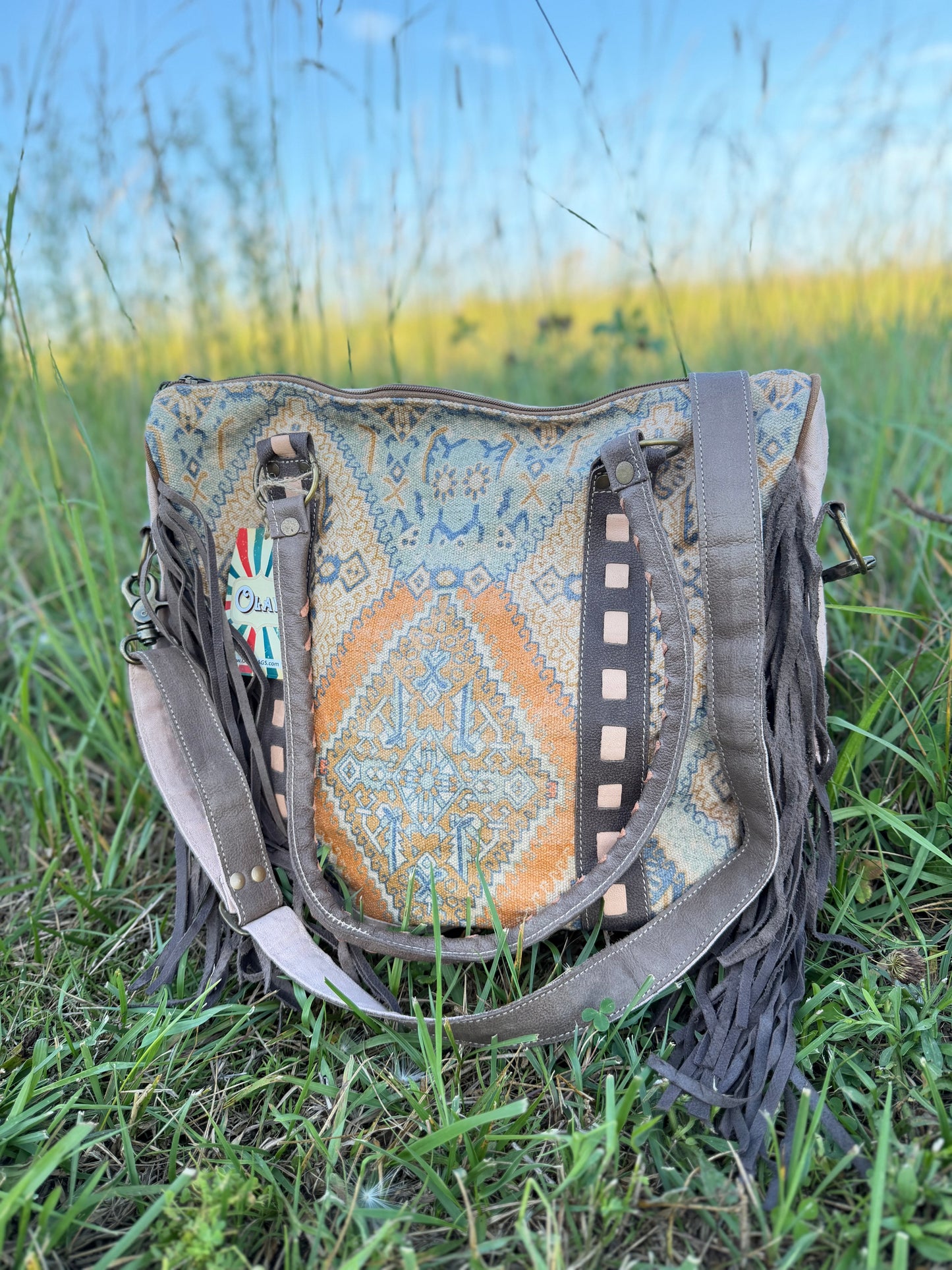 Handbag with patterned flap and fringes on grass
