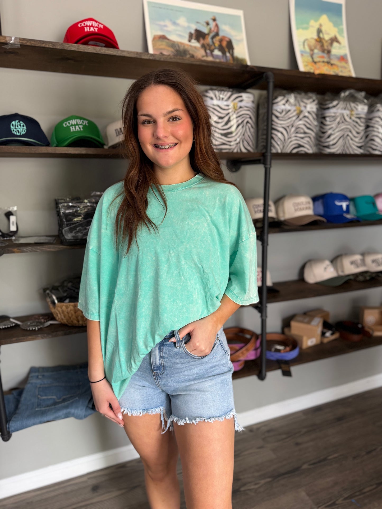 Woman in a store wearing a green t-shirt and denim shorts, with shelves of merchandise in the background.