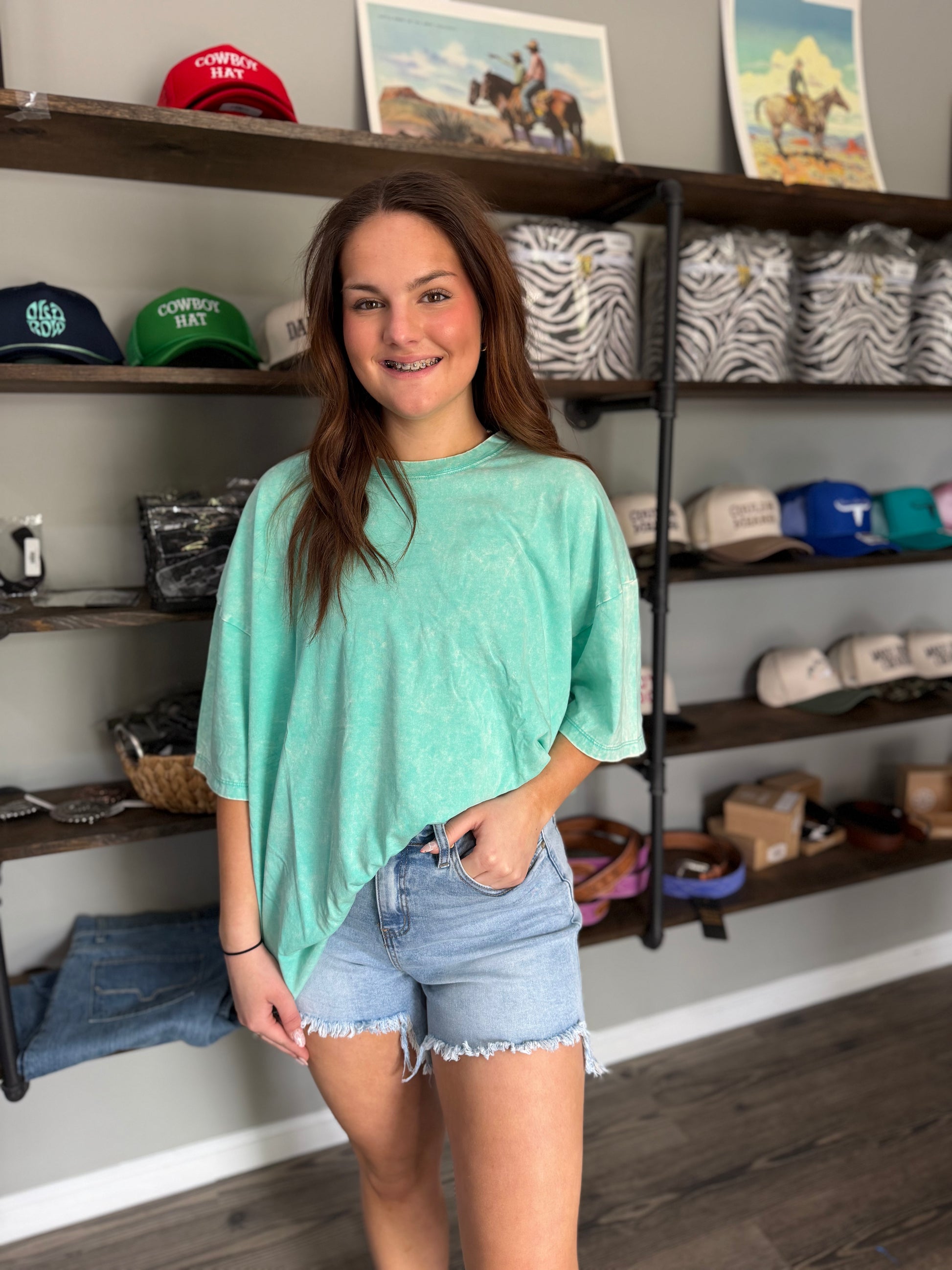 Woman in a store wearing a green t-shirt and denim shorts, with shelves of merchandise in the background.