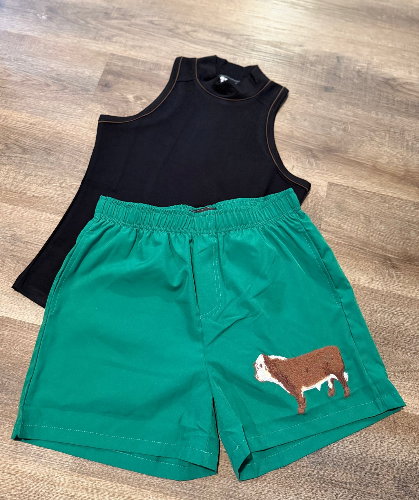 Black sleeveless top and green shorts with a cow design on a wooden floor.