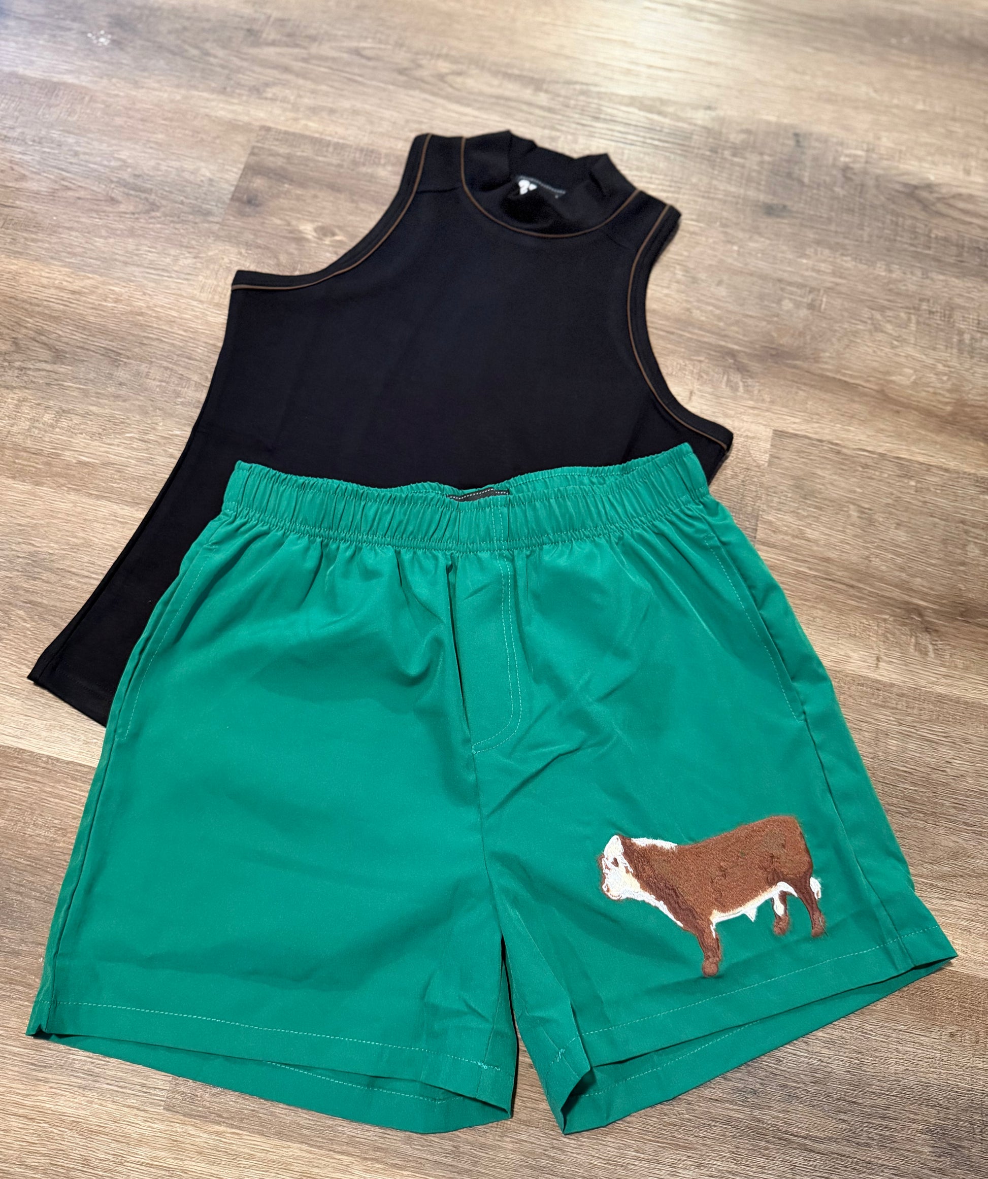 Black sleeveless top and green shorts with a cow design on a wooden floor.