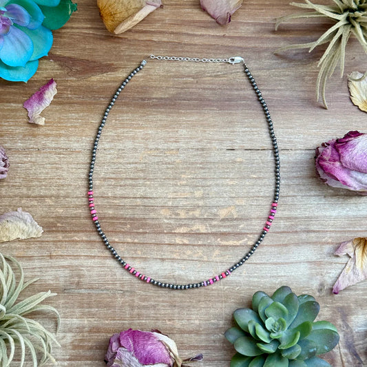 Necklace with black and pink beads on a wooden surface with flowers and succulents.