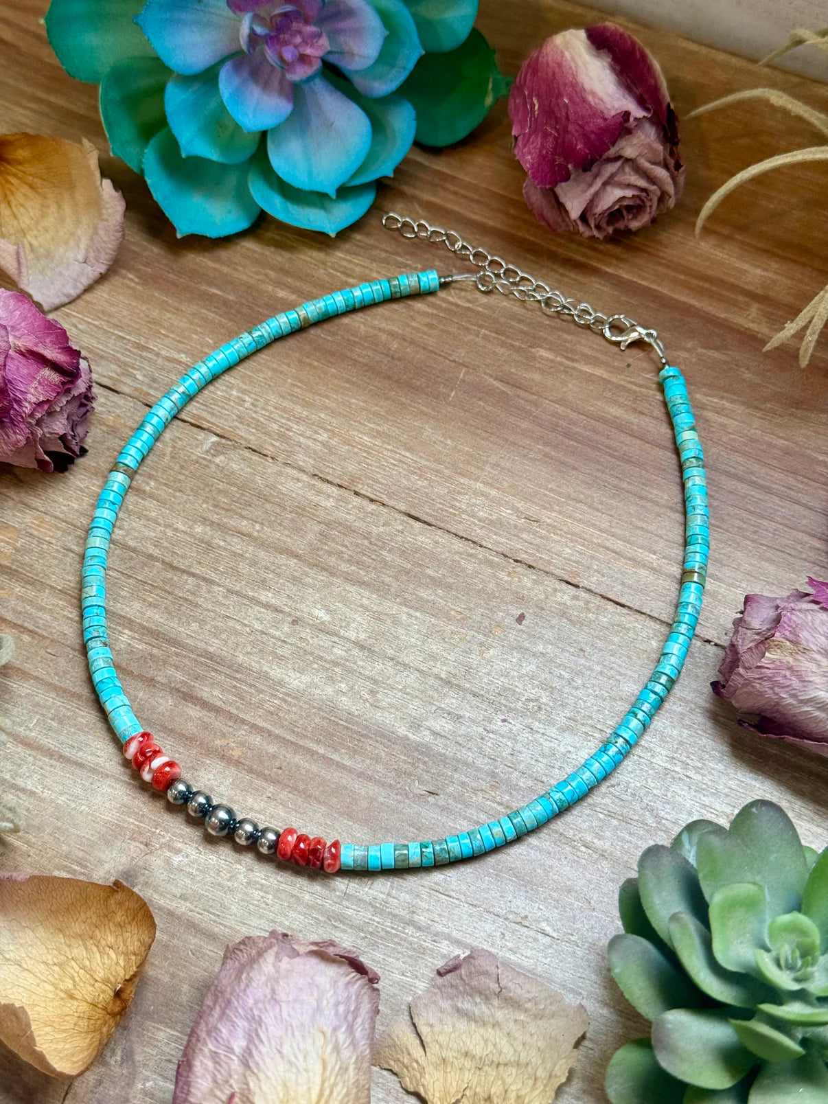 Turquoise beaded necklace on a wooden surface with flowers and succulents.