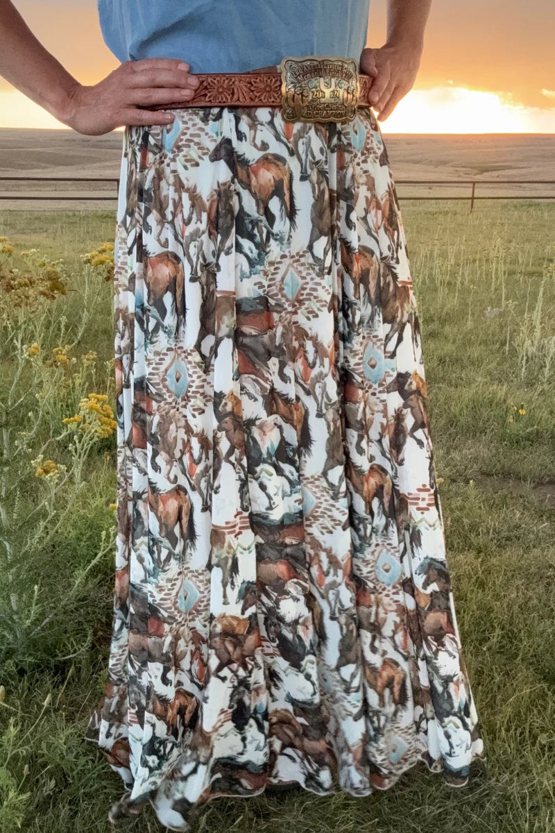 Person wearing a long, patterned skirt with a belt in a grassy field.