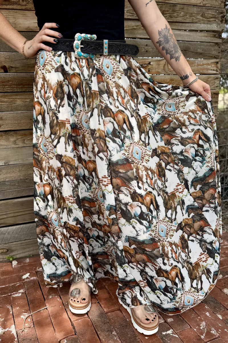 Person wearing a long skirt with horse print and a belt, standing on a wooden floor.