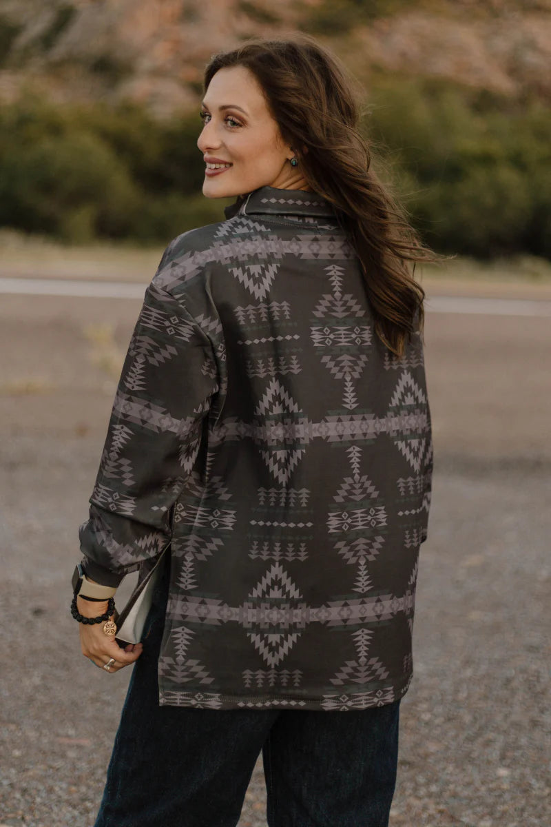 A woman wearing a dark gray long-sleeve button-up shirt with a light gray geometric southwestern pattern, photographed outdoors on a gravel path with a blurred natural background.