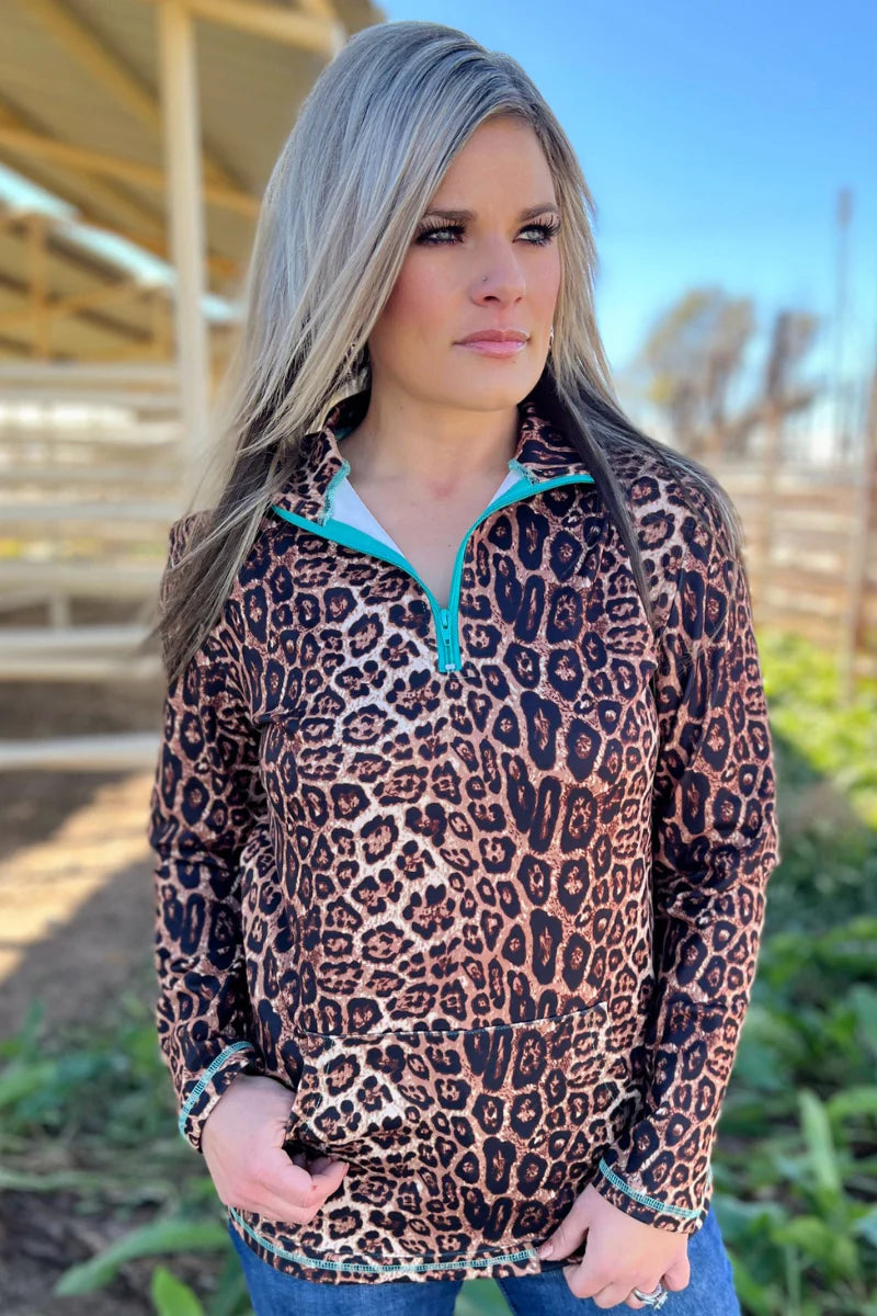 Woman wearing a leopard print pullover with turquoise lining outdoors.